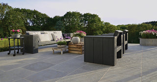 Outdoor patio with furniture, plants, and a grill on a stone patio.