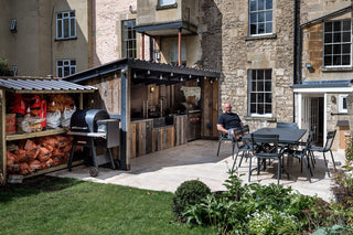 Outdoor patio area with barbecue, dining table, and chairs in a garden setting.