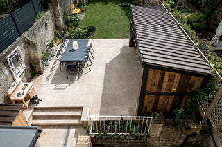 Outdoor patio area with external stone flooring, a dining table and chairs, stone steps, and a wooden structure.