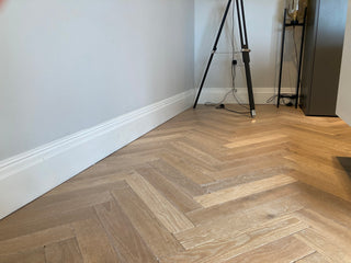 Wooden floor with a herringbone pattern in a room with a tripod and small table.